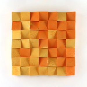 May include: A wall art piece made of wood squares in shades of orange and yellow. The squares are arranged in a grid pattern and have a slightly raised texture.