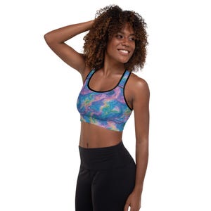 May include: A sports bra with a colorful, swirling pattern in shades of blue, purple, and yellow. The bra has black trim and straps. The model is wearing black leggings.