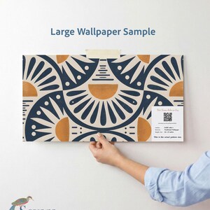 May include: A large wallpaper sample featuring a repeating geometric pattern of dark blue fan shapes and orange semi-circles on a cream background. The sample includes a white label with a QR code, text, and the dimensions 28 x 22 inches.