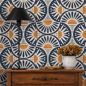 May include: A wooden console table with a single drawer and metal handle, topped with a black lamp and a white vase containing dried flowers. The background features wallpaper with a repeating pattern of dark blue and gold semicircular sunbursts.