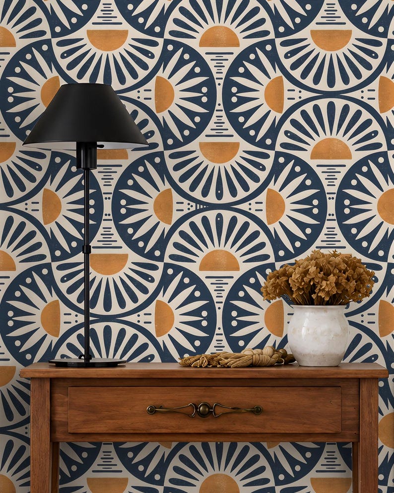 May include: A wooden console table with a single drawer and metal handle, topped with a black lamp and a white vase containing dried flowers. The background features wallpaper with a repeating pattern of dark blue and gold semicircular sunbursts.