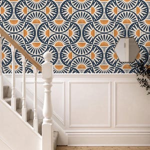 May include: Wallpaper featuring a repeating geometric pattern of dark blue and white semicircles with orange sun-like accents. The design is applied to a wall above white wainscoting, adjacent to a white wooden staircase and a small hexagonal mirror.