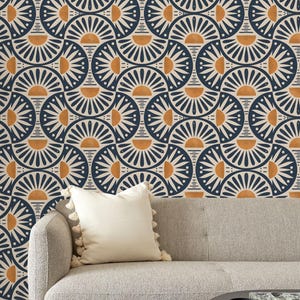 May include: A light gray sofa with a cream-colored throw pillow featuring tassels, positioned against a wall covered in wallpaper with a repeating geometric pattern of dark blue, cream, and orange semicircles and sunburst motifs.