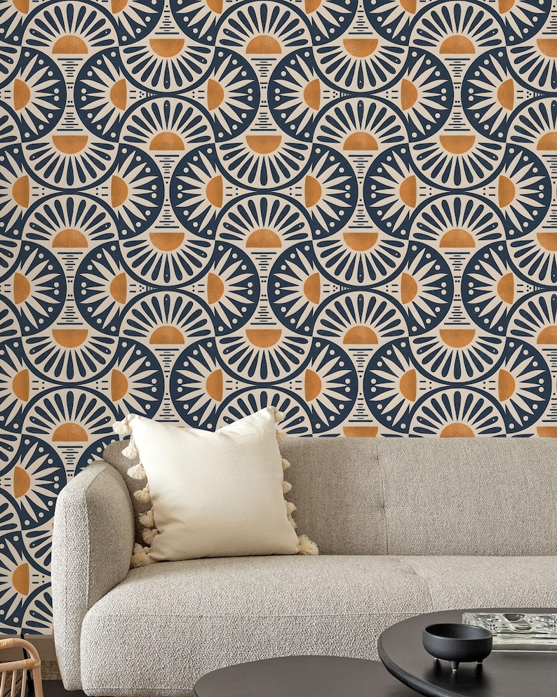 May include: A light gray sofa with a cream-colored throw pillow featuring tassels, positioned against a wall covered in wallpaper with a repeating geometric pattern of dark blue, cream, and orange semicircles and sunburst motifs.