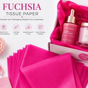 May include: A stack of fuchsia tissue paper sheets next to a white gift box filled with fuchsia tissue paper, a Biossance bottle, a Voluspa candle, and a Saint Luxe tube. A pink thank you card and pink ribbon are included in the display.