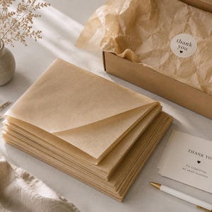 Peut inclure: Une pile de feuilles de papier de soie rectangulaires brun translucide, une boîte d'expédition en carton doublée de papier de soie froissé assorti avec un autocollant rond thank you, et une carte blanche avec le texte thank you for supporting my small business.