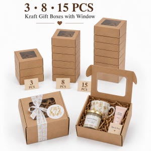 May include: Brown kraft gift boxes with clear windows, available in sets of 3, 8, or 15 pieces. The boxes feature a square design, with one example shown tied with a white patterned ribbon and another open, containing a candle, mug, and hand cream.