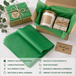 Peut inclure: Une pile de feuilles de papier de soie vert vif à côté d'une boîte cadeau en carton contenant une bougie en verre et un savon rectangulaire. La boîte est doublée de papier de soie vert et une petite étiquette brune avec le texte thank you.