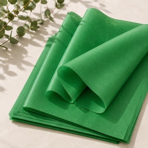 Peut inclure: Une pile de feuilles rectangulaires en papier de soie vert, fin et semi-transparent. Les feuilles supérieures sont pliées et drapées pour montrer la texture légère et délicate du papier. La couleur verte vive est uniforme sur toutes les couches.