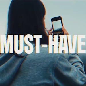Puede incluir: Una persona sostiene un smartphone, capturando una vista panorámica de un paisaje montañoso y brumoso. El texto "MUST-HAVE" está superpuesto en la imagen. La escena se desarrolla al aire libre con una paleta de colores suaves.