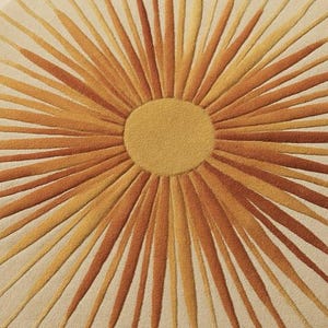 Puede incluir: Una alfombra redonda con un dise&ntilde;o de sol. El centro es de color amarillo-dorado s&oacute;lido, con l&iacute;neas radiantes en tonos naranja y amarillo-anaranjado sobre un fondo crema. La alfombra tiene un aspecto suave y texturizado.