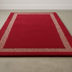 Peut inclure: Un tapis rectangulaire rouge avec une bordure tissée dans une nuance plus claire de rouge. Le tapis est posé sur un sol de couleur neutre, et la bordure ajoute un détail contrastant au centre rouge uni.