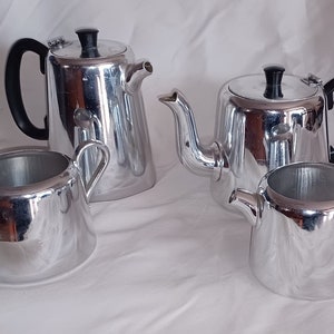 May include: A silver tea set comprising a teapot, creamer and sugar bowl. The set is made of polished aluminium and has a modern design.