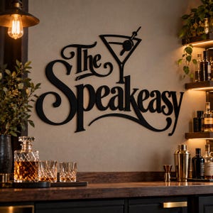 May include: A black metal wall sign featuring the text The Speakeasy in a decorative script font, accompanied by a martini glass icon with an olive. The sign is mounted on a wall, displaying clean lines and a matte finish for a bold visual impact.