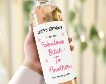 以下が含まれることがあります： ピンクのラベルが付いた白ワインのボトル。ラベルには「Happy Birthday from one Fabulous Bitch to Another」とピンクの星が書かれています。ラベルには「your message here」というテキストも書かれています。
