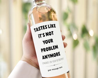 Puede incluir: Una botella de vino transparente con una etiqueta rosa que dice "TASTES LIKE IT'S NOT YOUR PROBLEM ANYMORE". La botella tiene una tapa rosa y está llena de un líquido rosa claro. La etiqueta también dice "CONGRATS ON YOUR RETIREMENT" y "your message here".