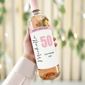 Puede incluir: Una botella de vino blanco con una etiqueta rosa que dice "Feliz cumpleaños" y "50" en un círculo rosa. La etiqueta también dice "Michelle" y "Tu mensaje aquí".