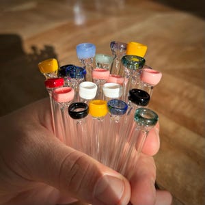 Puede incluir: Una colecci&oacute;n de pipas para fumar de vidrio con puntas de vidrio de colores. Las puntas son de varios colores, incluyendo rojo, azul, verde, amarillo y rosa.