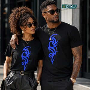 May include: Two black short-sleeved t-shirts featuring a vibrant blue tribal-style graphic print on the front. The shirts have a crew neckline and a standard fit. A small logo with the text ZINYLU is visible in the upper right corner of the image.