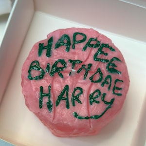 May include: Pink birthday candle with green icing that says "Happy Birthday Harry".