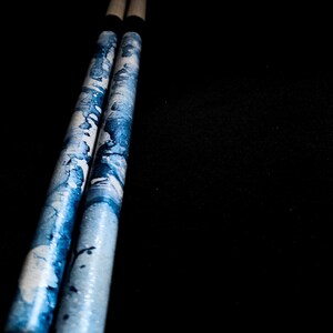 May include: A pair of blue and white drumsticks with a black grip.