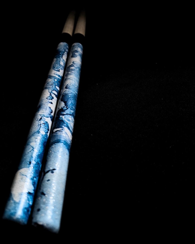 May include: A pair of blue and white drumsticks with a black grip.