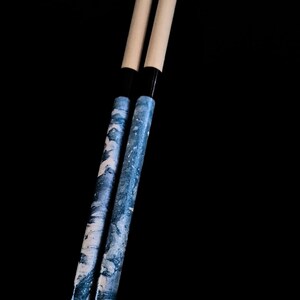 May include: Two wooden drumsticks with a blue and white marbled design. The drumsticks have black tips.