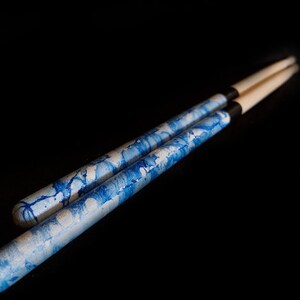 May include: Two wooden drumsticks with a blue and white marbled design. The drumsticks have black rubber tips.