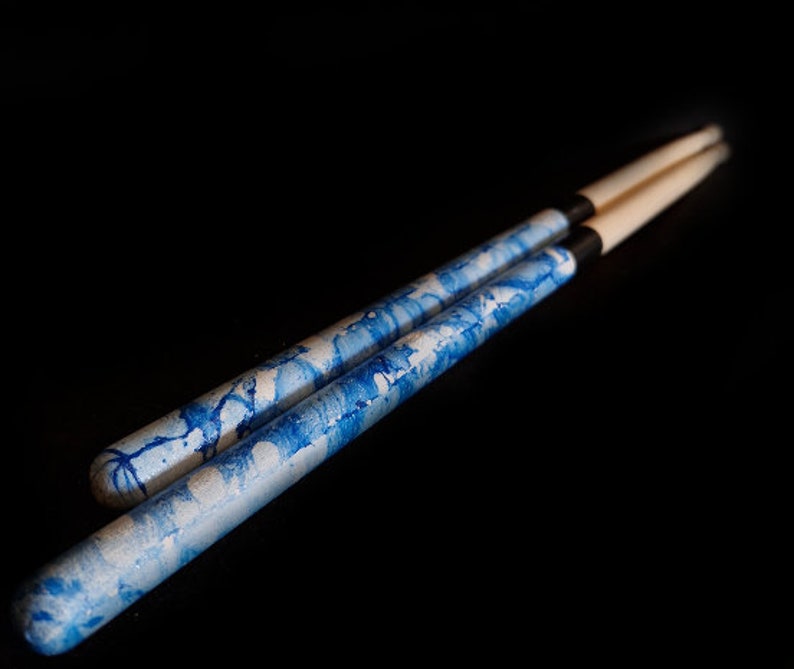 May include: Two wooden drumsticks with a blue and white marbled design. The drumsticks have black rubber tips.
