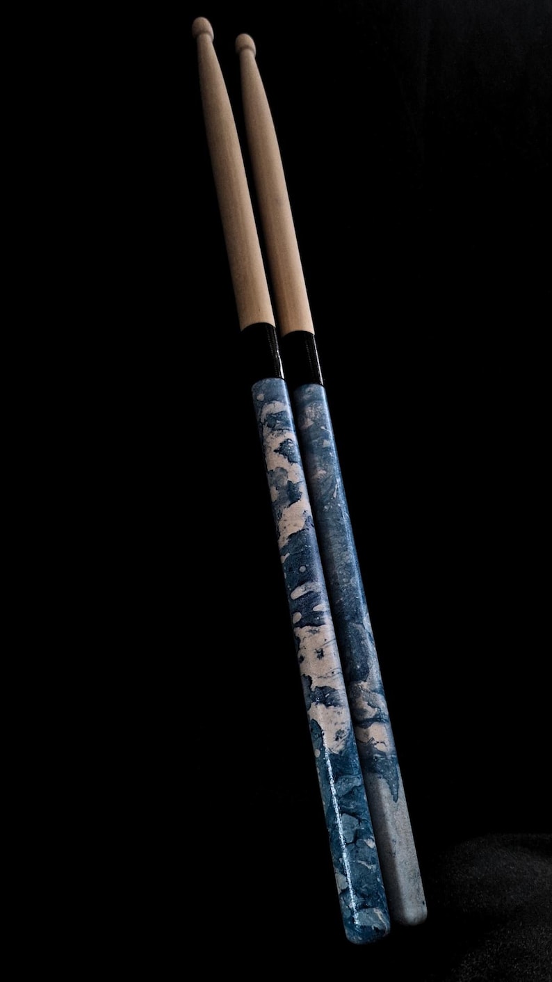 May include: Two wooden drumsticks with a blue and white marbled design. The drumsticks have black tape near the top.