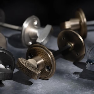May include: A selection of door knobs in diverse metallic finishes, including bronze, silver, and black. The knobs feature varied handle designs, some with hammered textures. The image has a shallow depth of field, highlighting the details of the hardware.