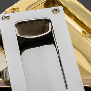 May include: Close-up of two recessed cabinet pulls. One is polished chrome, rectangular with rounded edges, and the other is gold-toned. Both have a rectangular recessed handle area and mounting holes.