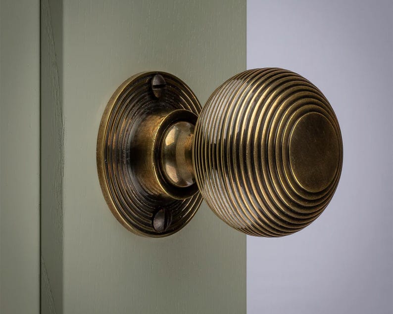 K&ouml;nnte beinhalten: Nahaufnahme eines T&uuml;rknaufs aus Messing mit rundem, gerilltem Design. Der Knauf ist an einer hellgr&uuml;nen T&uuml;r angebracht. Die kreisf&ouml;rmige R&uuml;ckplatte ist ebenfalls aus Messing und hat ein geriffeltes Muster. Die Hardware hat eine Vintage-&Auml;sthetik.