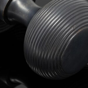 May include: Close-up of a dark, possibly antique, door knob. The knob is a deep, matte black with a ribbed, circular design. The metal appears to have a slight sheen, reflecting the light. The design suggests a vintage or classic style.