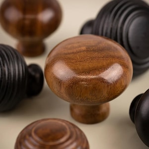 May include: A selection of wooden cabinet knobs in shades of brown and black. The knobs vary in shape, including round and mushroom designs. Some have a smooth finish, while others feature a grooved texture.