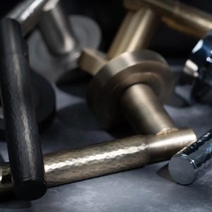 May include: A selection of metal door handles in various finishes, including black, brass, and silver. The handles have a hammered texture and are arranged on a dark surface. The image showcases a selection of hardware.