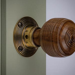 May include: A wooden door knob with a brass backplate and accents. The knob is a warm brown colour with concentric circular grooves. The backplate is circular with a ridged design and is attached to a light green door.