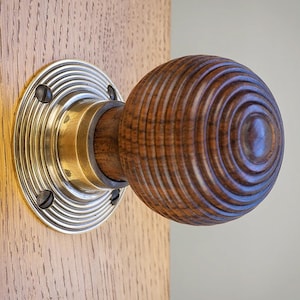 May include: A wooden door knob with a circular design, attached to a wooden door. The knob is a warm brown colour with concentric rings. The metal plate is silver-coloured. The door knob is approximately 7 cm in diameter.