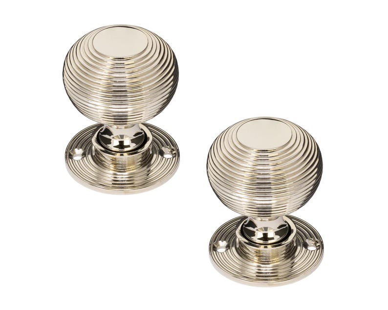 K&ouml;nnte beinhalten: Zwei T&uuml;rkn&ouml;pfe aus poliertem Nickel. Jeder Knopf hat eine kugelf&ouml;rmige Form mit konzentrischen Rillen und einer kreisf&ouml;rmigen Basis. Die Beschl&auml;ge sind aus Metall und haben eine gl&auml;nzende, reflektierende Oberfl&auml;che. F&uuml;r eine T&uuml;r.