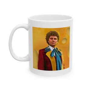 May include: White ceramic mug with a colorful illustration of a person with curly hair wearing a red, yellow, and blue patterned jacket. The background is a yellow and white abstract design.