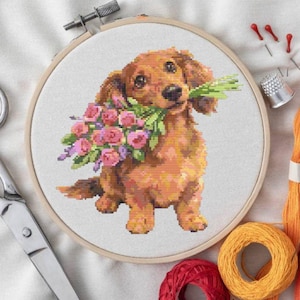 May include: A cross-stitch embroidery hoop featuring a dachshund dog holding a bouquet of pink and purple flowers. The dog is brown with long fur. Embroidery supplies, including scissors, needles, and colorful thread, surround the hoop.