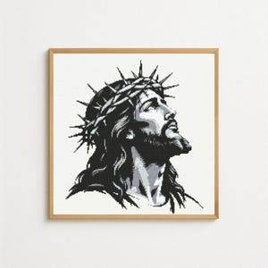 Può includere: Un ritratto in bianco e nero incorniciato di un uomo con una corona di spine, che guarda in alto. L'opera d'arte è un'immagine pixelata con uno sfondo chiaro e una cornice di legno. L'uomo ha i capelli lunghi e la barba.