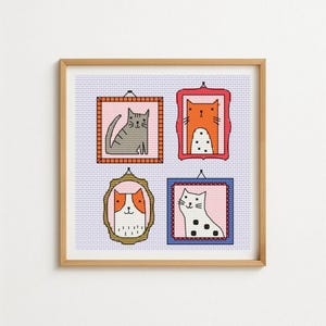 May include: A framed artwork featuring four cross-stitch cat portraits. Each cat is in a different frame, with varying colors and designs. The artwork has a light blue background and a wooden frame.
