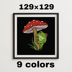 May include: Framed cross-stitch art featuring a green frog under a red and white mushroom. The artwork is set against a black background. The text "129x129" and "9 colors" are displayed on the image.