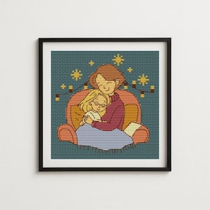 May include: A framed cross-stitch art piece depicting a mother and child embracing. The mother wears a burgundy sweater and the child is in a white shirt and glasses. The background is teal with star and light string details. The frame is black.