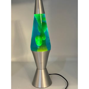 May include: A retro lava lamp with a silver base and a conical glass container. The lamp contains blue liquid with green wax that flows when heated. The lamp has a black power cord.