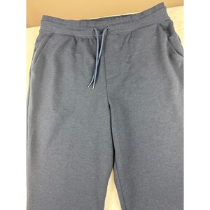 May include: Dark navy blue sweatpants with a drawstring waist and side pockets. The pants are made of a soft, comfortable material, perfect for casual wear. The drawstring is a lighter shade of blue.