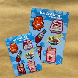 Puede incluir: Dos hojas de pegatinas con ilustraciones temáticas de comida sobre un fondo azul. Las pegatinas representan un pollo de dibujos animados, tofu, una botella de salsa, un cuenco de fideos y paquetes de Pocky. El texto "Rood Food Series 1" y "By Cheekee Stickees" son visibles.