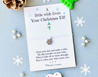 May include: A white card with the text "A little wish from Your Christmas Elf!" and a snowflake charm bracelet. The card includes instructions and is surrounded by snowflake and heart decorations, and a pinecone.