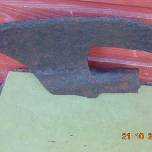 May include: A rusty, dark gray metal axe with a curved blade and a wooden handle. The axe is resting on a green surface with the date 21 10 2018 written on it.